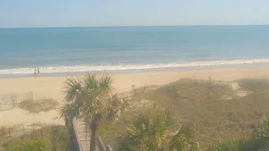 Live webcam offering gorgeous views of Ocean Isle Beach, NC showing sandy shoreline, marina boats, and the Intracoastal Waterway under a sunny sky.
