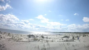 Live webcam view of Cape May, NJ beach showing sandy shoreline, gentle ocean waves, and beachgoers enjoying a sunny day with colorful umbrellas and blue skies.