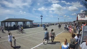 Ocean City NJ boardwalk view with beach in the background and patrons walking, biking, and enjoying shops along the busy boardwalk.