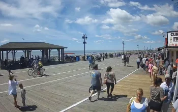 Ocean City NJ boardwalk view with beach in the background and patrons walking, biking, and enjoying shops along the busy boardwalk.