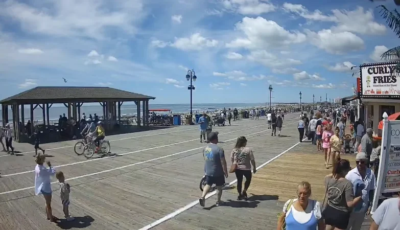 Ocean City NJ boardwalk view with beach in the background and patrons walking, biking, and enjoying shops along the busy boardwalk.