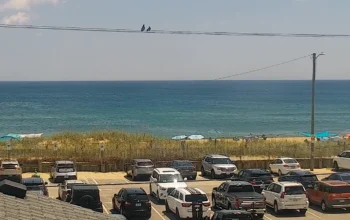 Beachfront view from Shutters on the Banks hotel in Kill Devil Hills, North Carolina, showing soft sand, ocean waves, and a clear blue sky.