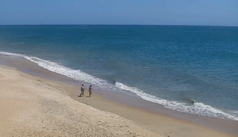 Live view of Buxton NC Beach showing gentle ocean waves, sandy shoreline, and clear skies along the Outer Banks coast
