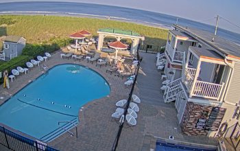 Live webcam view of Cliff House in York, Maine, showing the rocky Atlantic coastline, ocean waves crashing below, and the resort perched on a seaside cliff under an open sky.