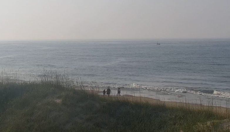 Frisco Woods Campground live cam view of the beach with ocean waves, sandy shoreline, and distant dunes under a clear sky