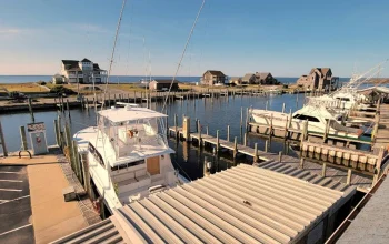 Scenic view of Hatteras, NC from Hatteras Harbor Marina showing docked charter boats, calm water, and coastal buildings under a clear blue sky