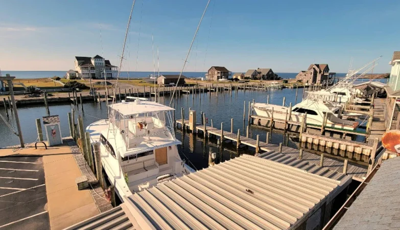 Scenic view of Hatteras, NC from Hatteras Harbor Marina showing docked charter boats, calm water, and coastal buildings under a clear blue sky
