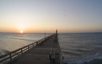 Ocean view from Rodanthe Pier, showcasing the Atlantic waves rolling toward the sandy shore with coastal cottages lining the Outer Banks horizon under a vivid sky