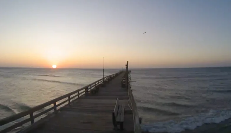 Ocean view from Rodanthe Pier, showcasing the Atlantic waves rolling toward the sandy shore with coastal cottages lining the Outer Banks horizon under a vivid sky
