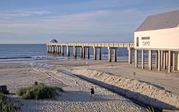 A vibrant view of Surfside Beach, South Carolina, showing the sandy shoreline, gentle ocean waves, and the Surfside Beach Pier extending over the water under a clear blue sky.