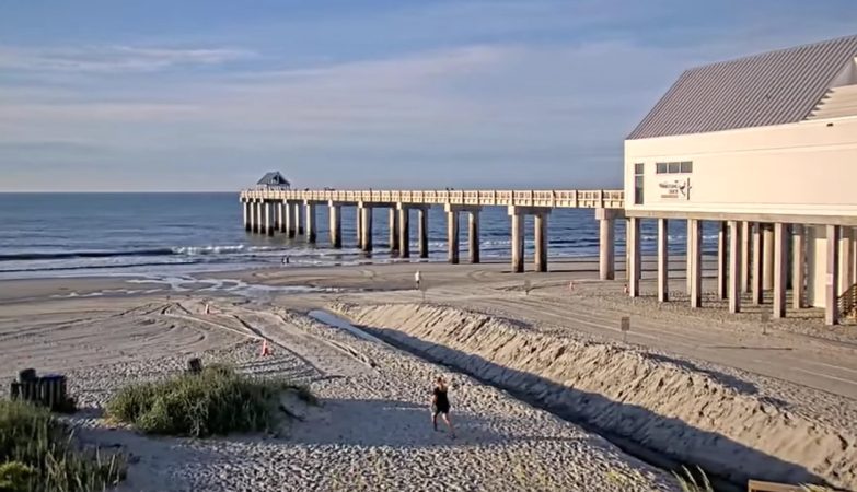 A vibrant view of Surfside Beach, South Carolina, showing the sandy shoreline, gentle ocean waves, and the Surfside Beach Pier extending over the water under a clear blue sky.