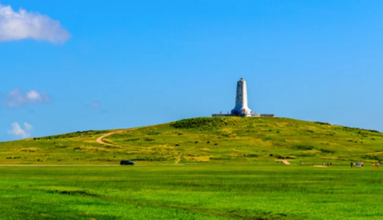 Scenic view of the Wright Brothers National Memorial in Kill Devil Hills, North Carolina, with the granite monument standing tall against a clear blue sky, commemorating the first powered flight.
