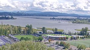 University of Washington live webcam view overlooking Lake Washington with calm blue water, tree-lined shores, and Seattle skyline in the distance.