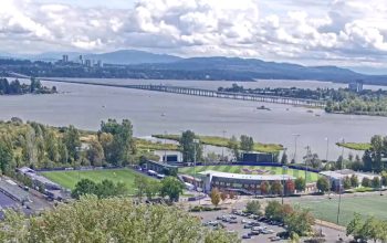 University of Washington live webcam view overlooking Lake Washington with calm blue water, tree-lined shores, and Seattle skyline in the distance.