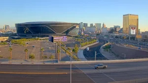 Allegiant Stadium exterior, home of the Las Vegas Raiders, with traffic flowing on the Las Vegas Freeway and Strip hotels in the distance