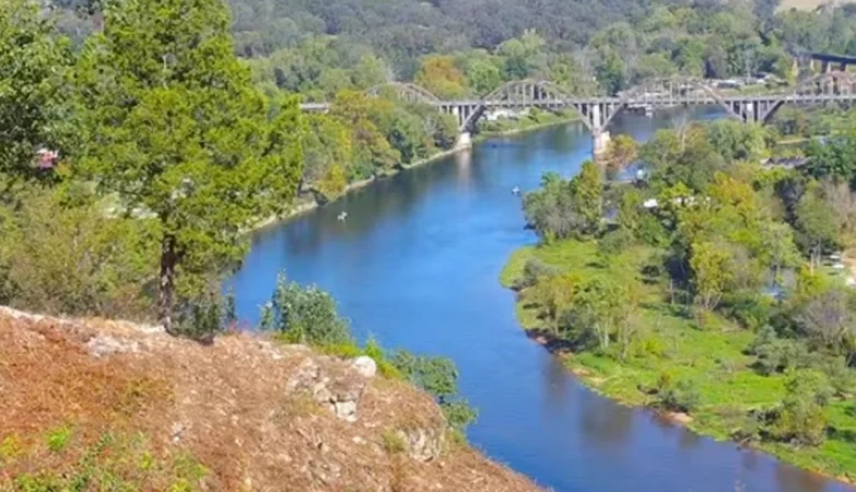 Historic Rainbow Bridge arching over the White River in Cotter, Arkansas, with calm water reflecting the concrete arches and surrounding Ozark greenery.