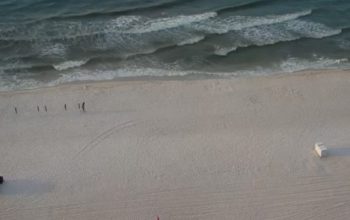 Sweeping beach view from a Phoenix IX balcony in Orange Beach, Alabama, showing white sand, gentle waves, and the Gulf stretching to the horizon.